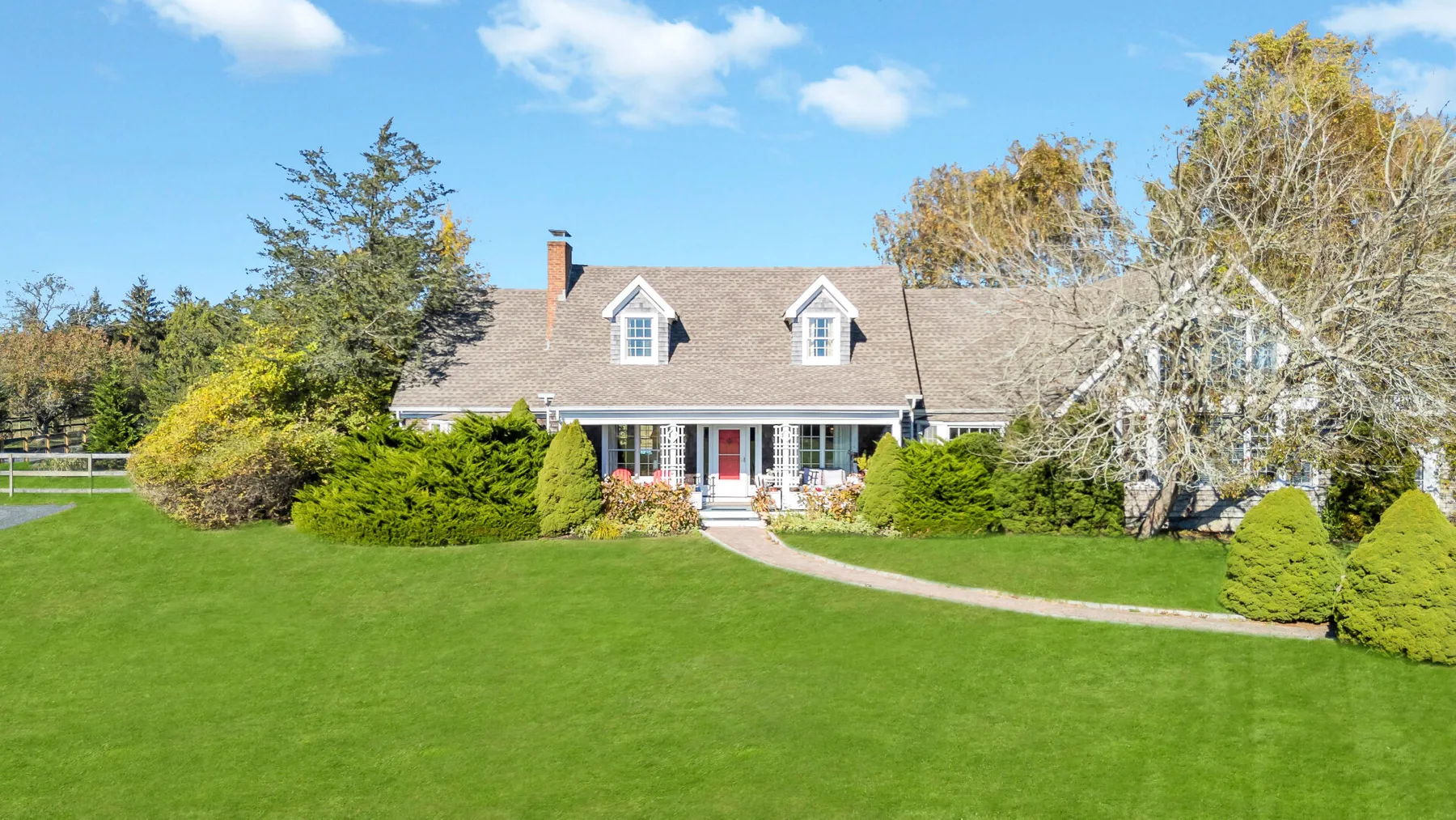 A house stands beyond a broad green lawn, with a curved path leading to the entrance.
