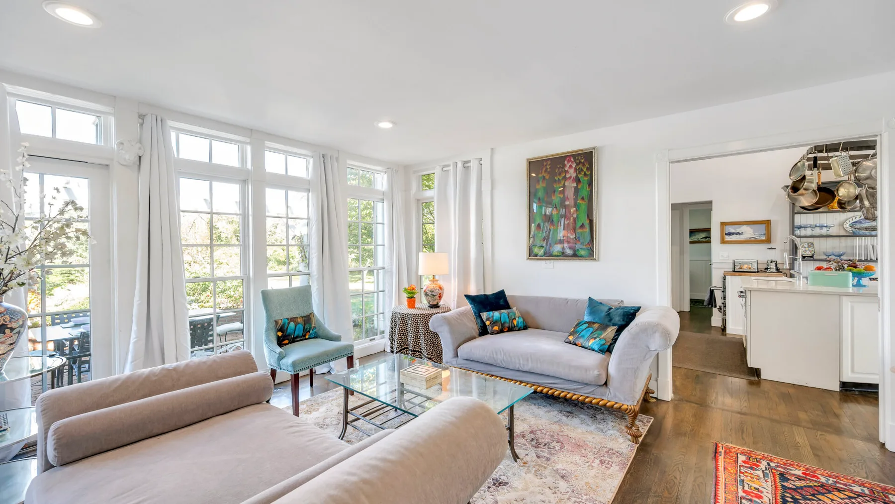 A bright living room with seating, large windows, and a glass coffee table.