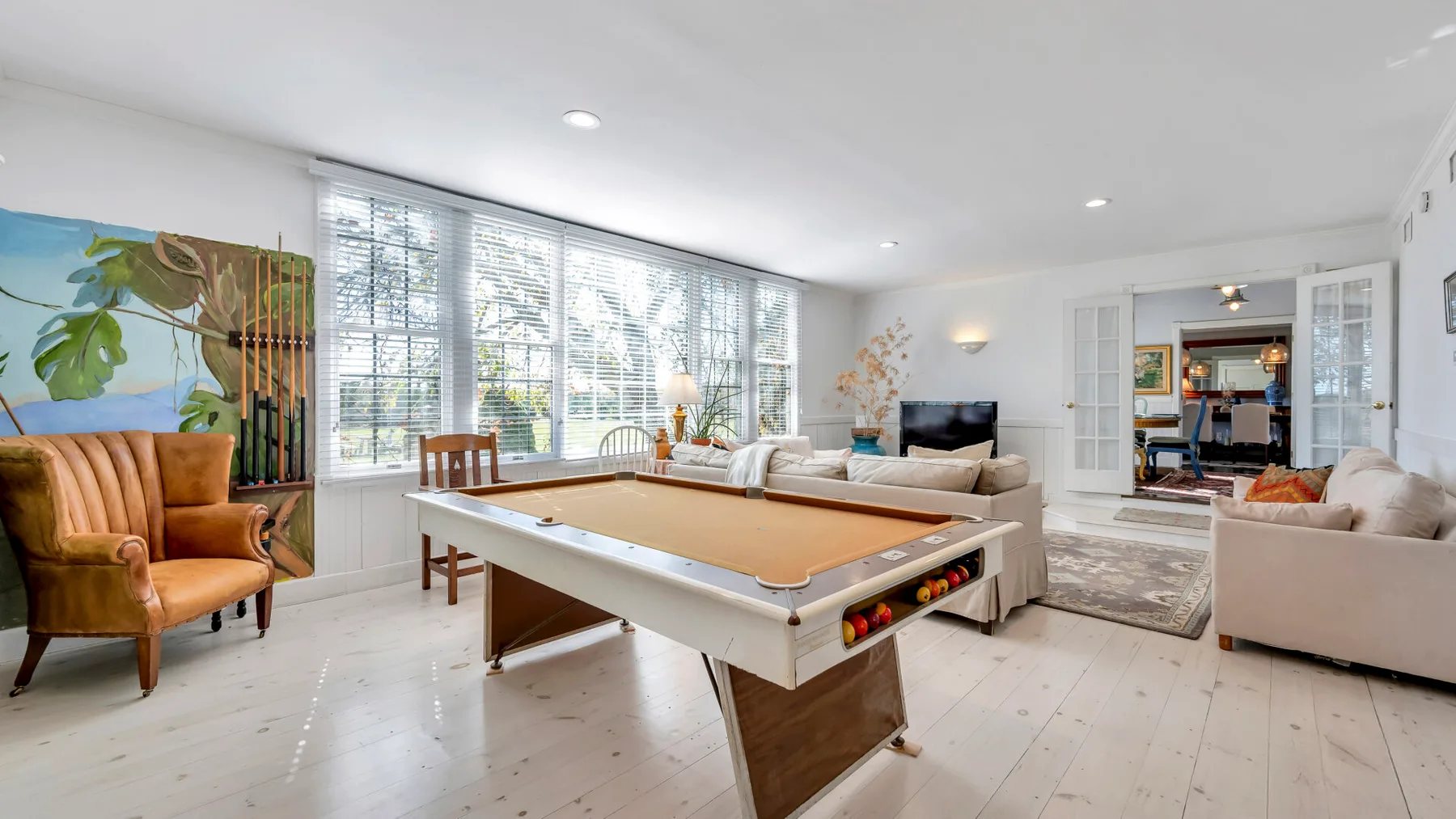 A bright living room with a pool table and seating beside large windows.