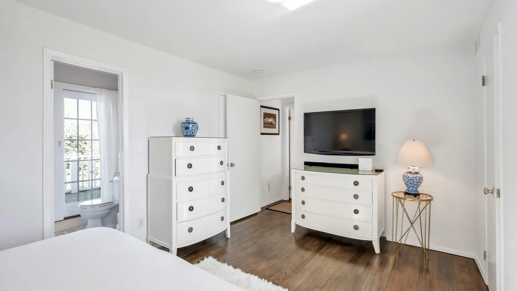 A bright bedroom with a bed, dressers, and a television.