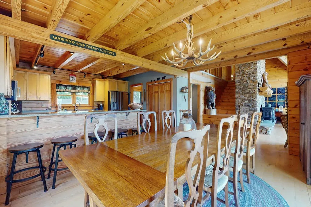A rustic dining area has a long wooden table beneath exposed timber beams.
