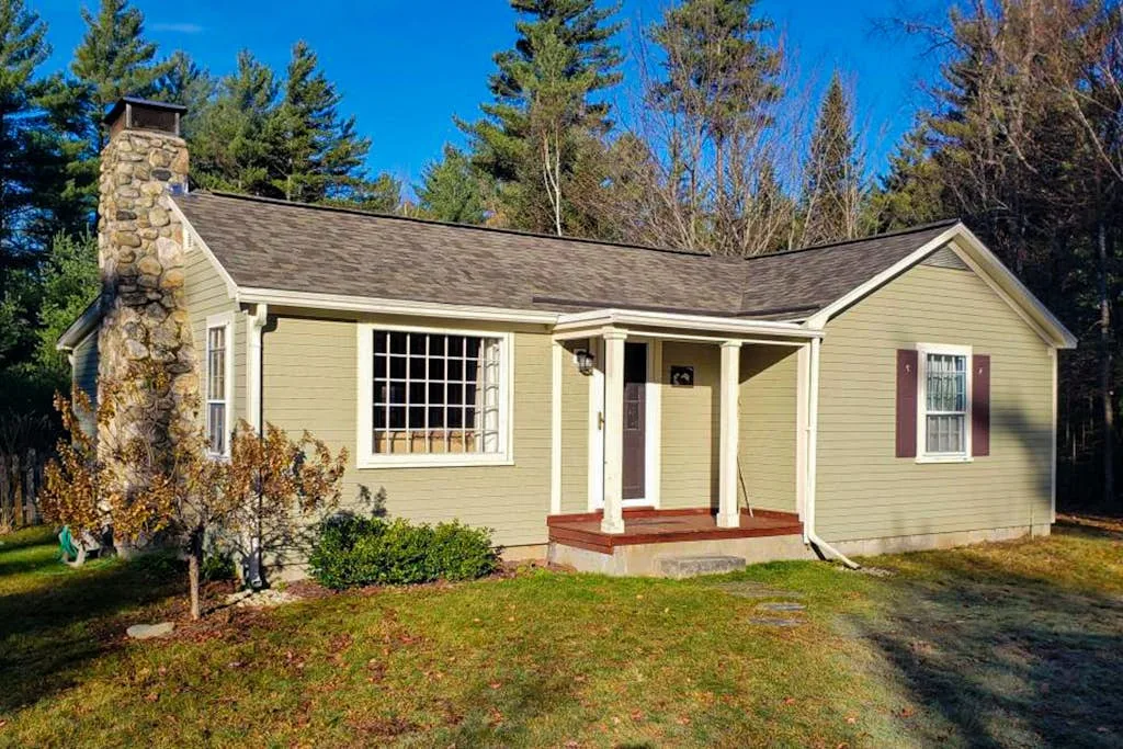 A single-story house with pale siding, a stone chimney, and a front porch.