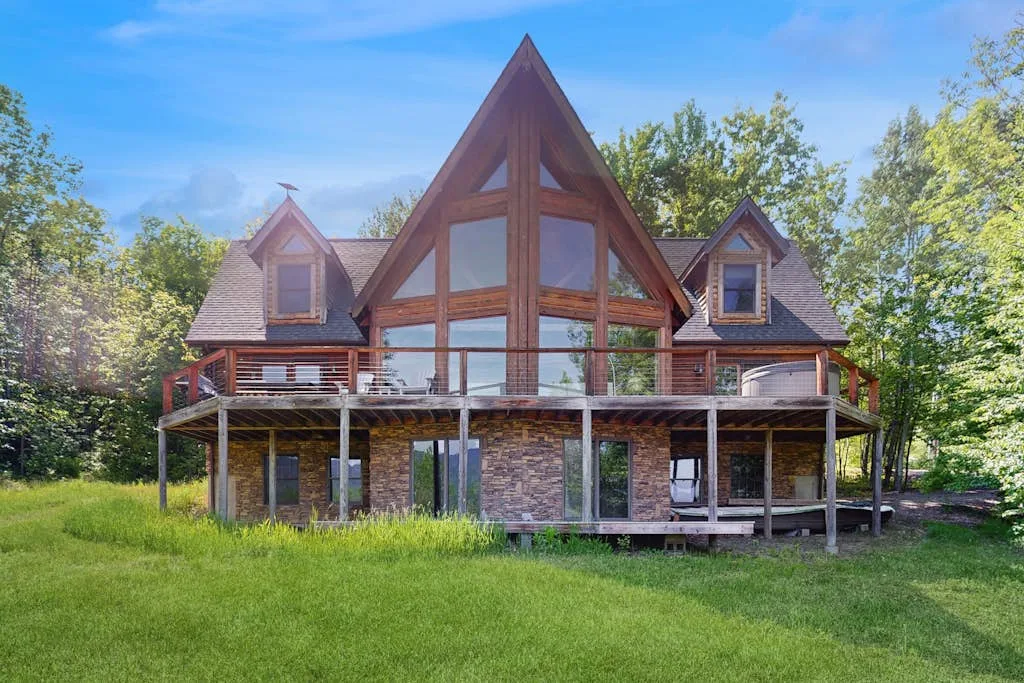 A large house with a steep central roof stands behind a grassy lawn.