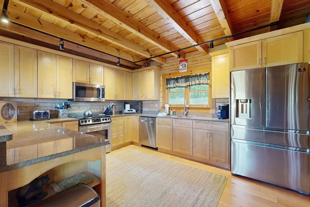 A kitchen with light cabinetry, stainless steel appliances, and a wood-paneled ceiling.