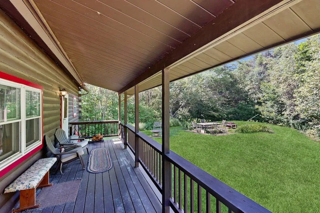A covered porch with outdoor seating overlooks a green lawn and trees.