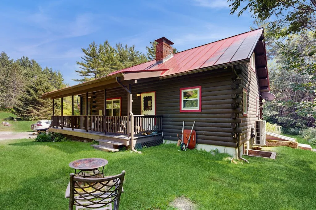 A log cabin with a covered porch sits beside a green lawn.