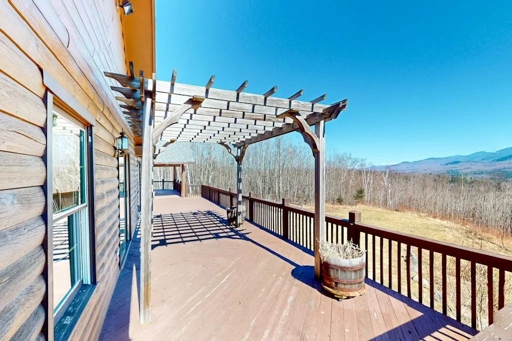 A wooden deck with a pergola and railing overlooks an open landscape.