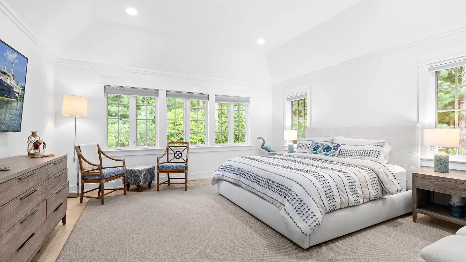 Un dormitorio luminoso con una cama grande, ventanas amplias y una pequeña zona de estar.