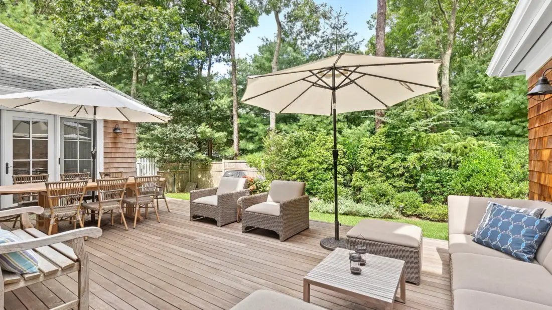 Una terraza exterior de madera tiene asientos, una mesa de comedor y una sombrilla grande.