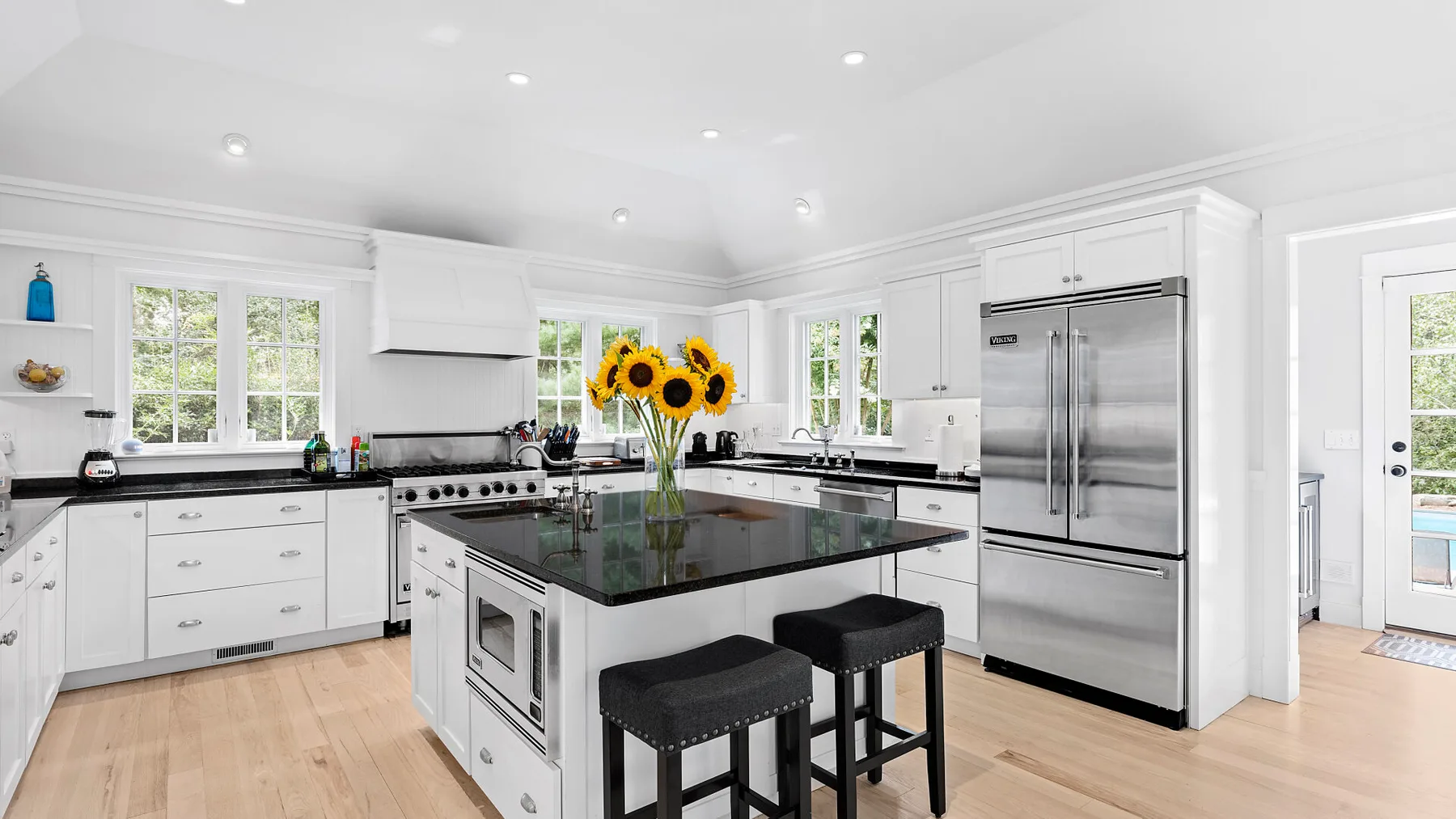 Cocina blanca y luminosa con una isla central, encimera oscura y electrodomésticos de acero inoxidable.
