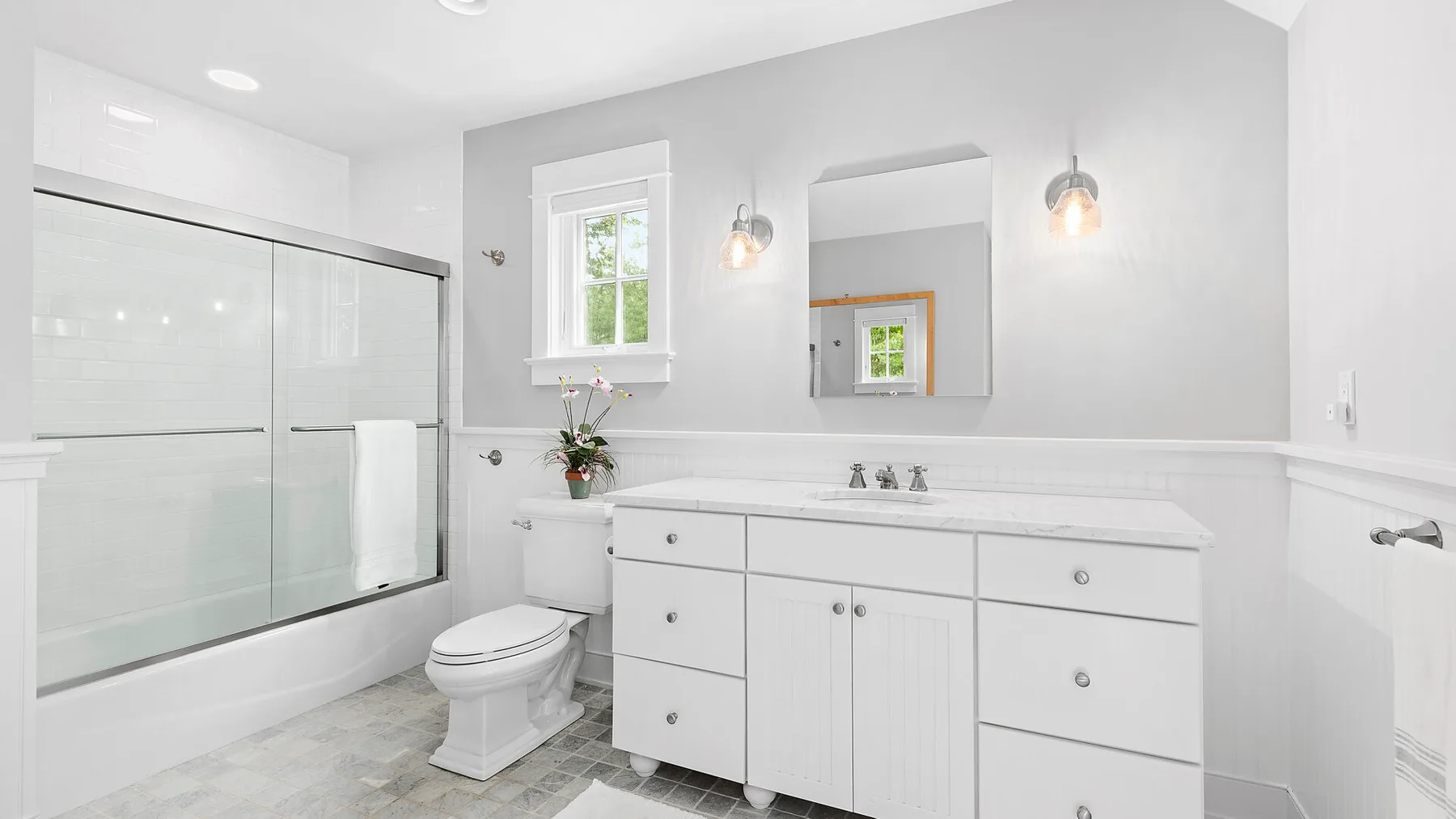 Un baño luminoso con ducha de vidrio, bañera y tocador blanco.
