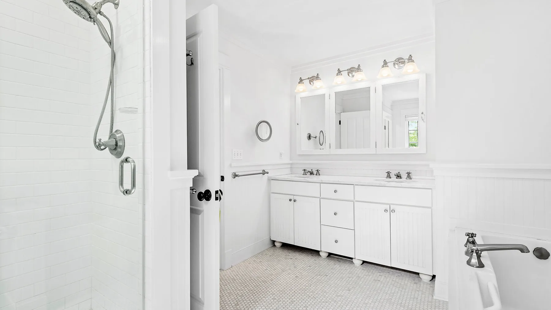 Un baño blanco y luminoso con un tocador largo, espejos y una ducha.