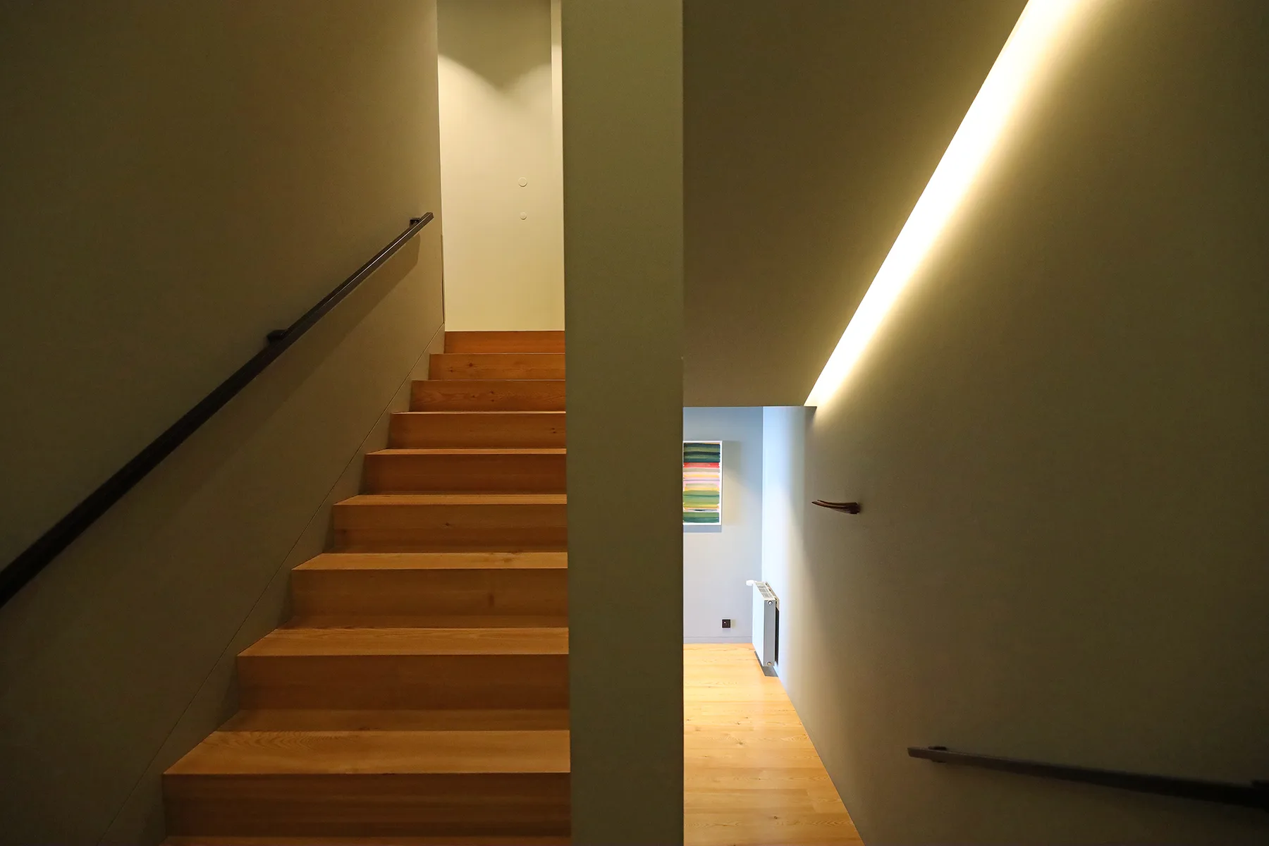 An indoor staircase with wooden steps leads toward a bright hallway.