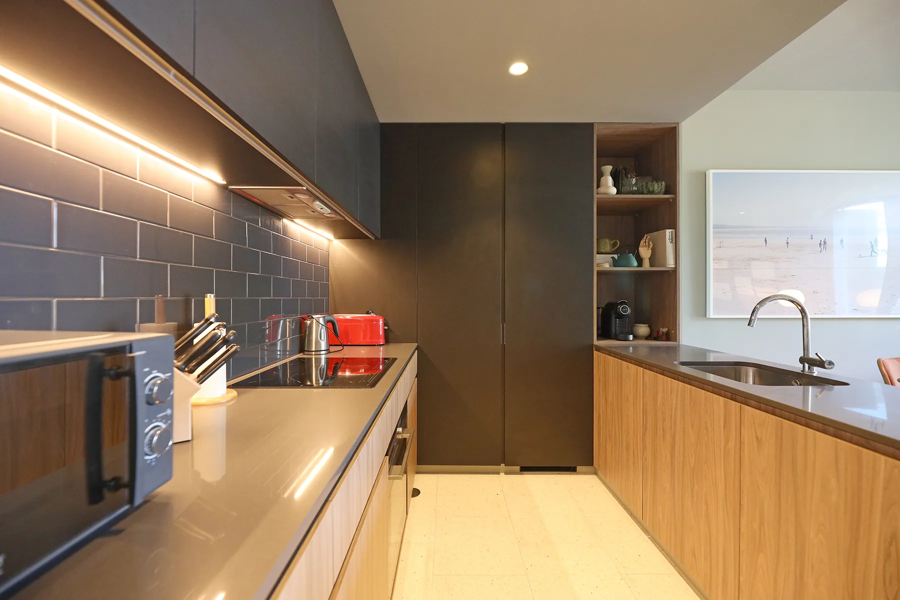 A modern kitchen with dark cabinets, wood-fronted counters, and a sink.