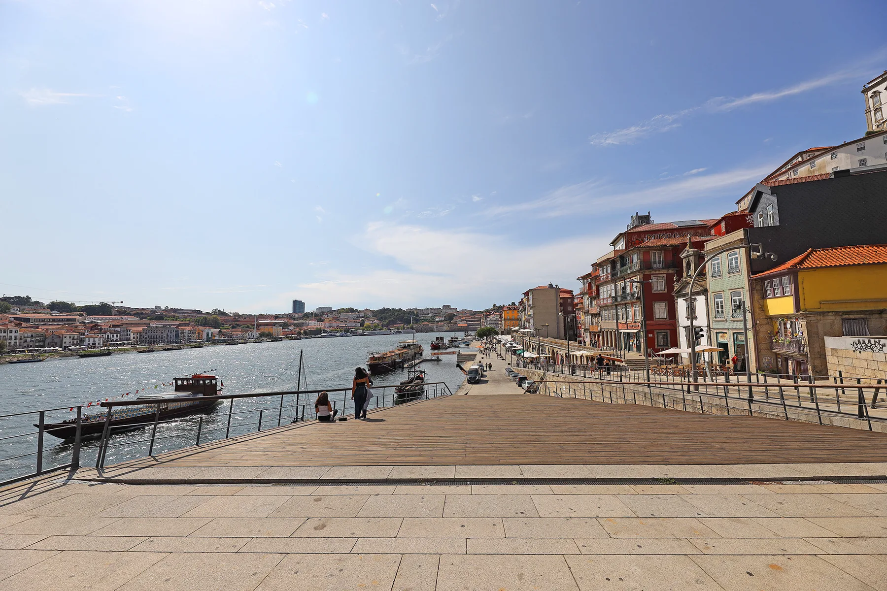 A paved riverside promenade overlooks the water and colorful buildings along the opposite bank.