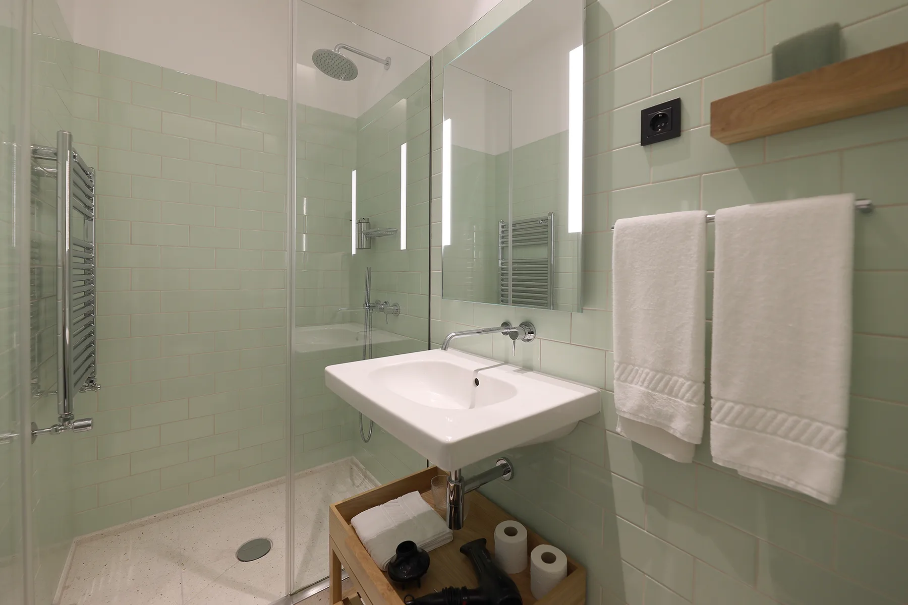 A tiled bathroom with a shower, sink, and towels.