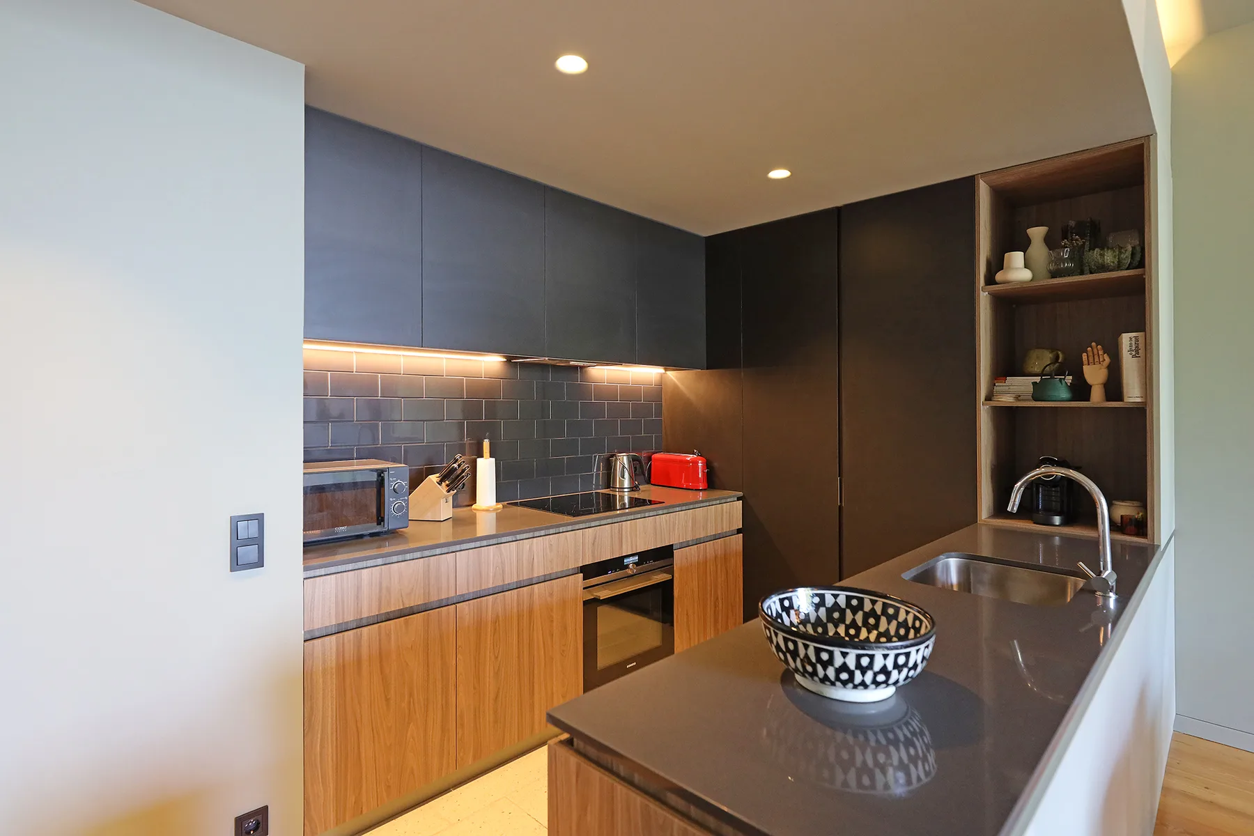 A modern kitchen with dark cabinets, wood-toned cupboards, and a countertop.