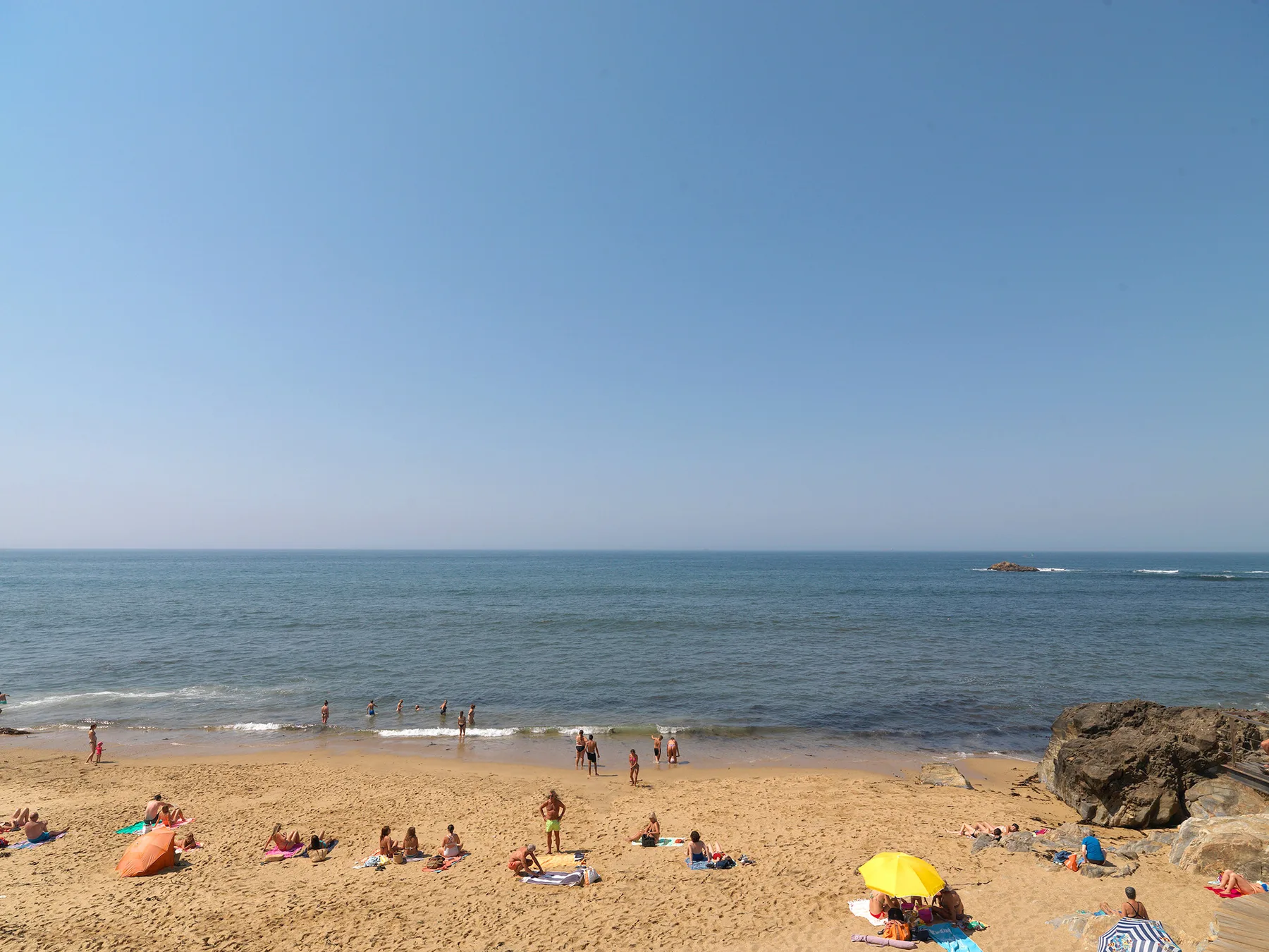 A sandy beach meets the sea, with people relaxing along the shore.