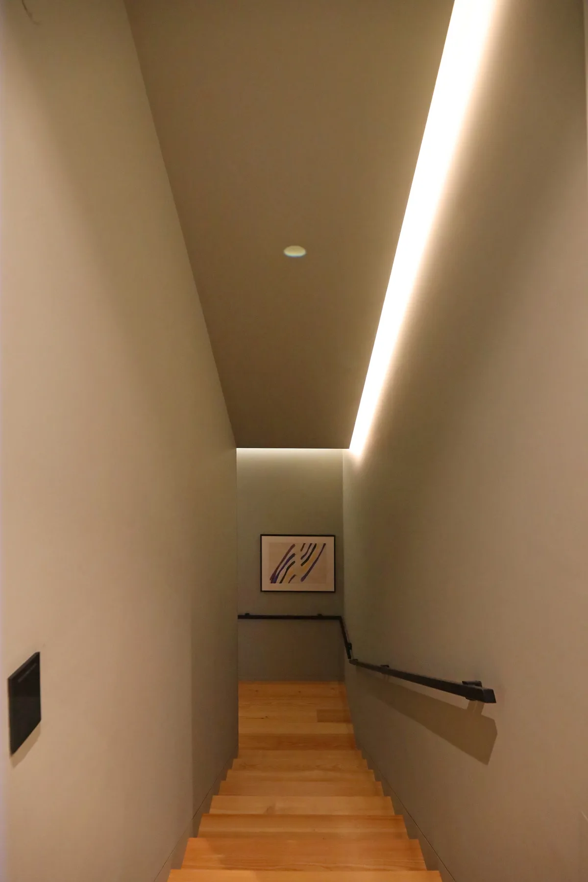 An indoor staircase descends between plain walls with a handrail.