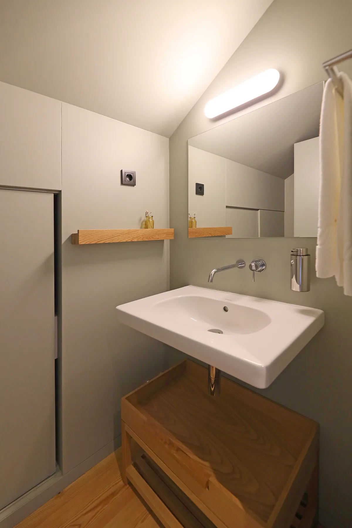 A bathroom with a wall-mounted sink, mirror, and wooden vanity.