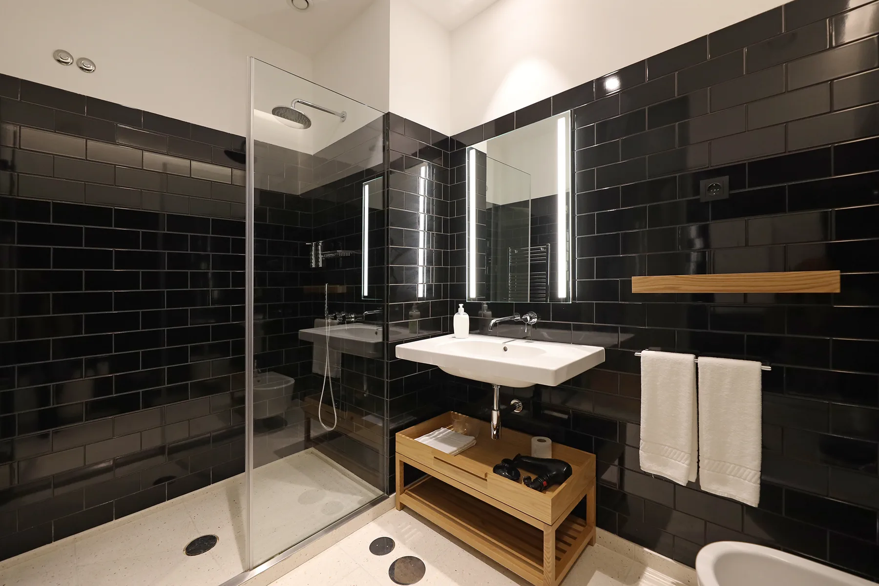 A bathroom with a glass shower, sink, and black tiled walls.