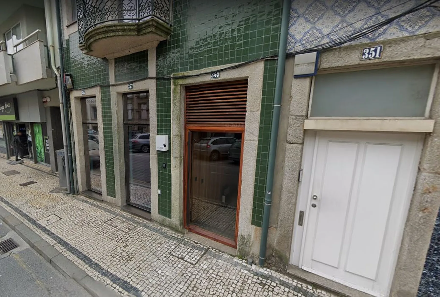 Street-facing building entrance with green tilework and a patterned stone sidewalk.