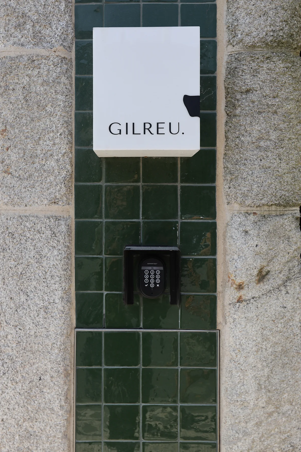 An exterior entrance wall has a name sign above a keypad.