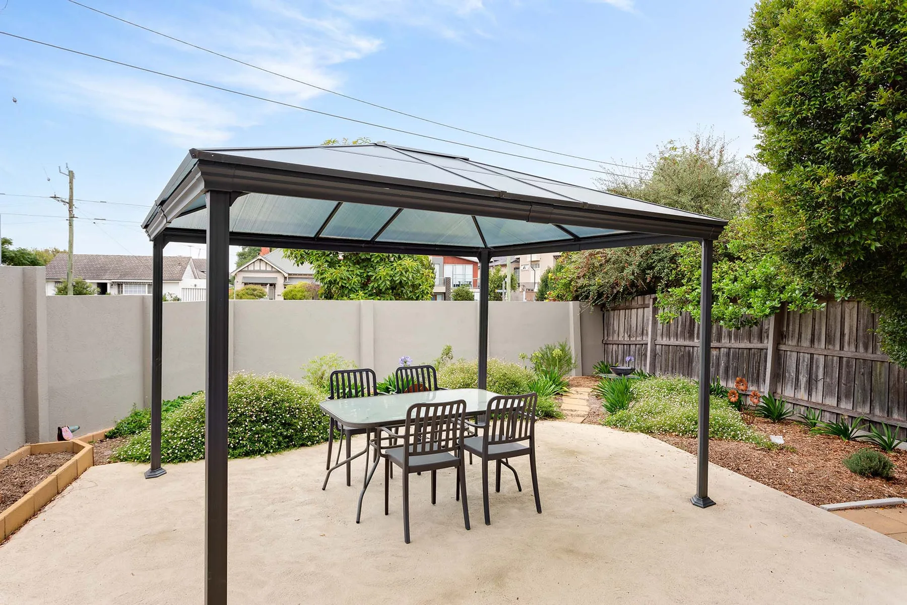 A covered outdoor dining area with a table and seating in a paved yard.