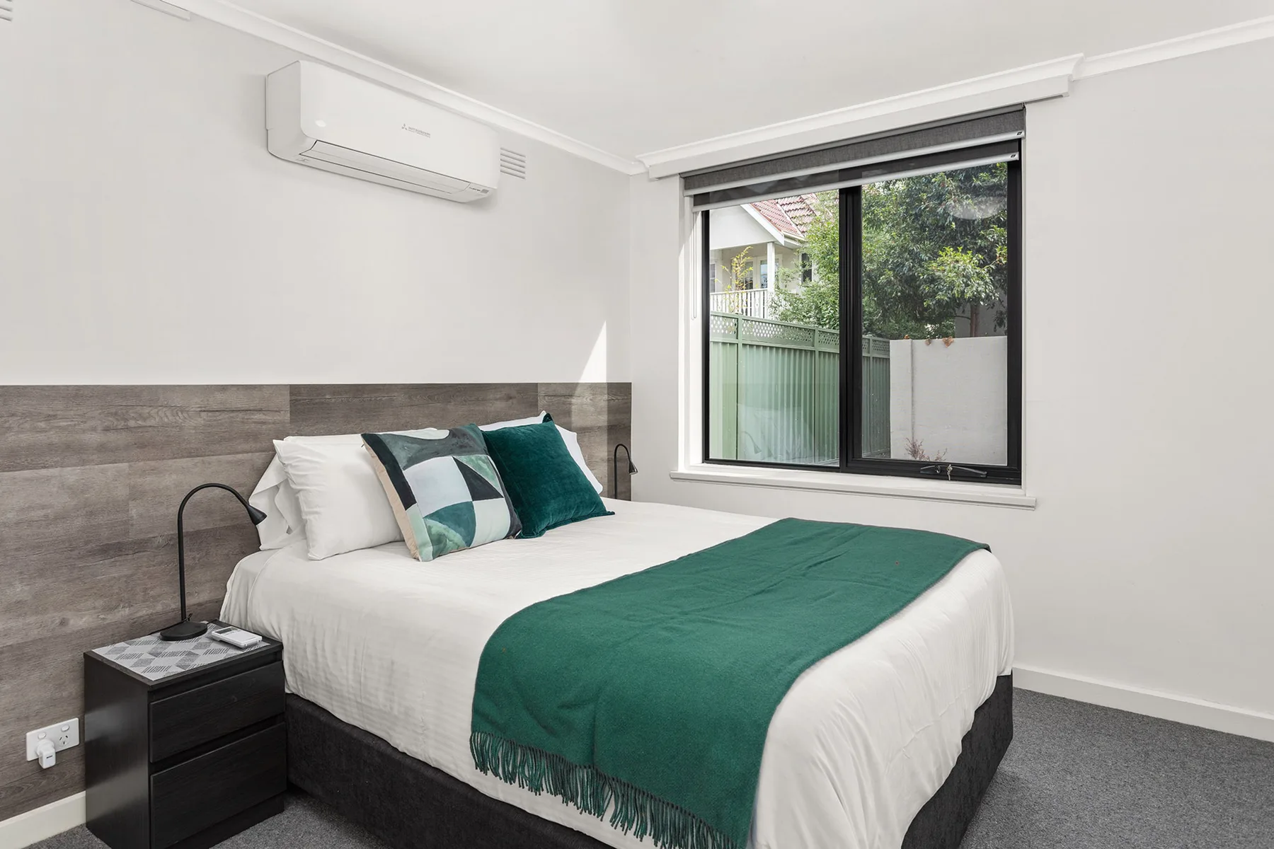A bedroom with a neatly made bed and a large window.