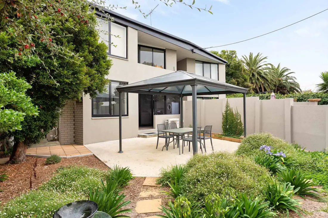 A paved outdoor patio with a covered seating area beside a garden.