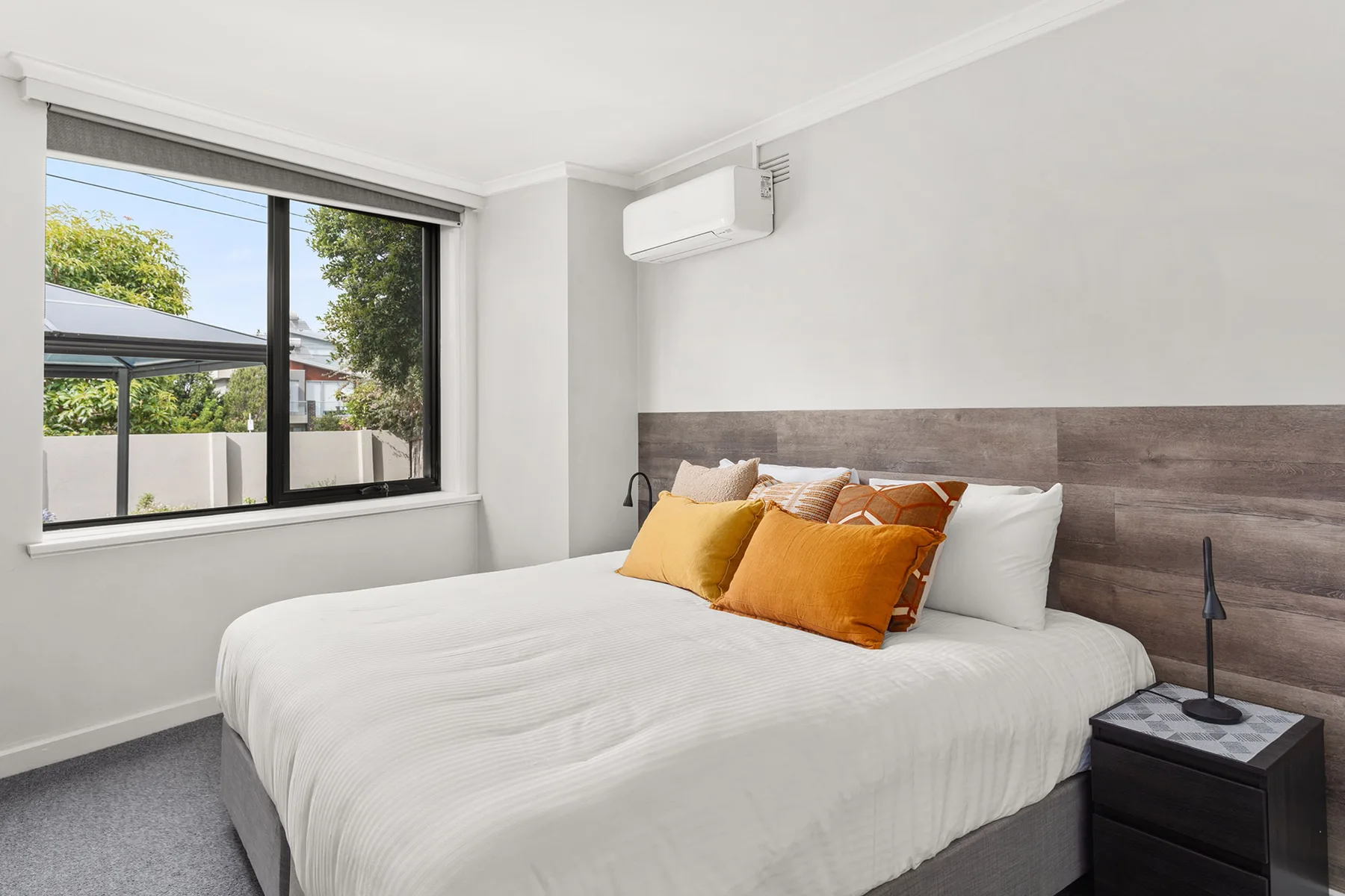 A bedroom with a bed, colorful pillows, and a large window.