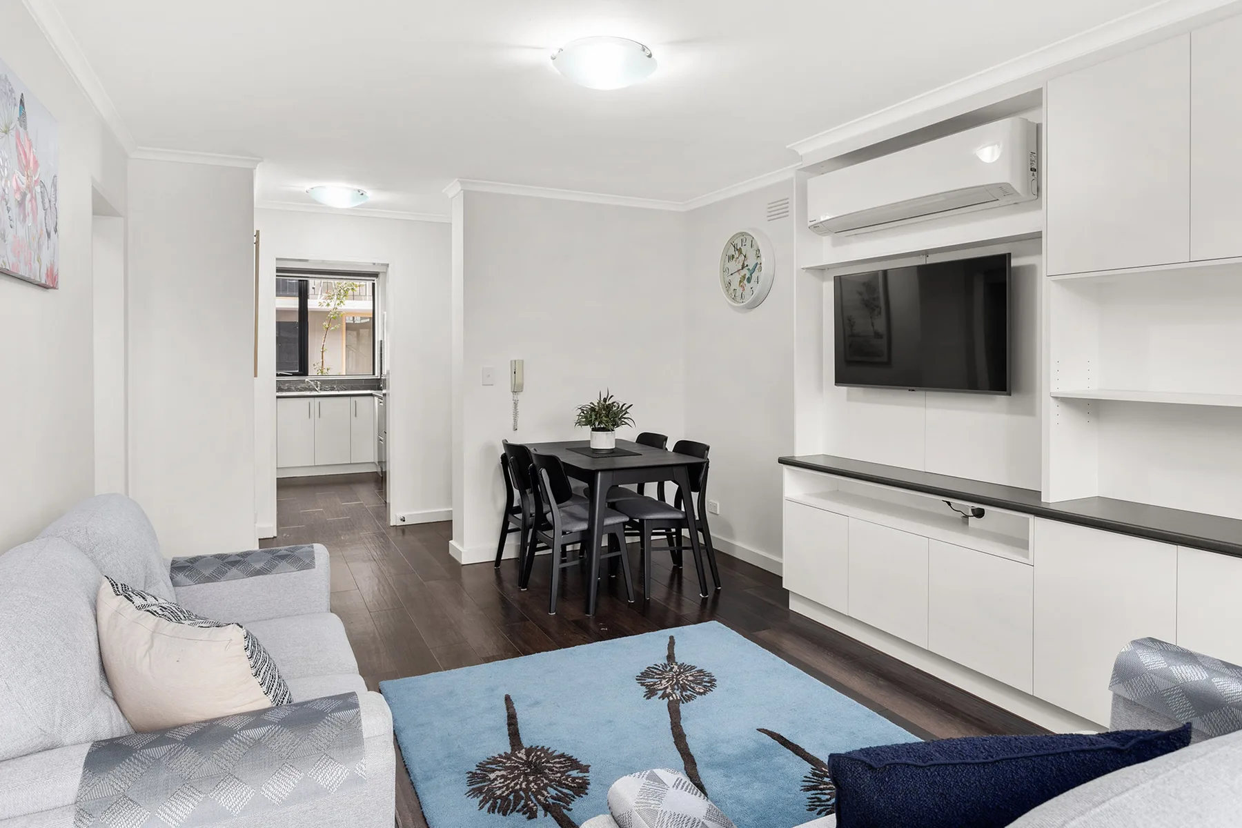 A bright living and dining area with seating, a table, and a wall-mounted television.
