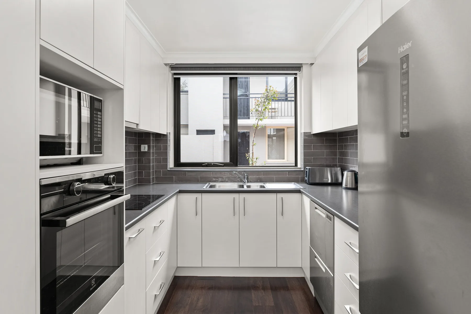 A bright kitchen with white cabinets, dark countertops, and stainless steel appliances.