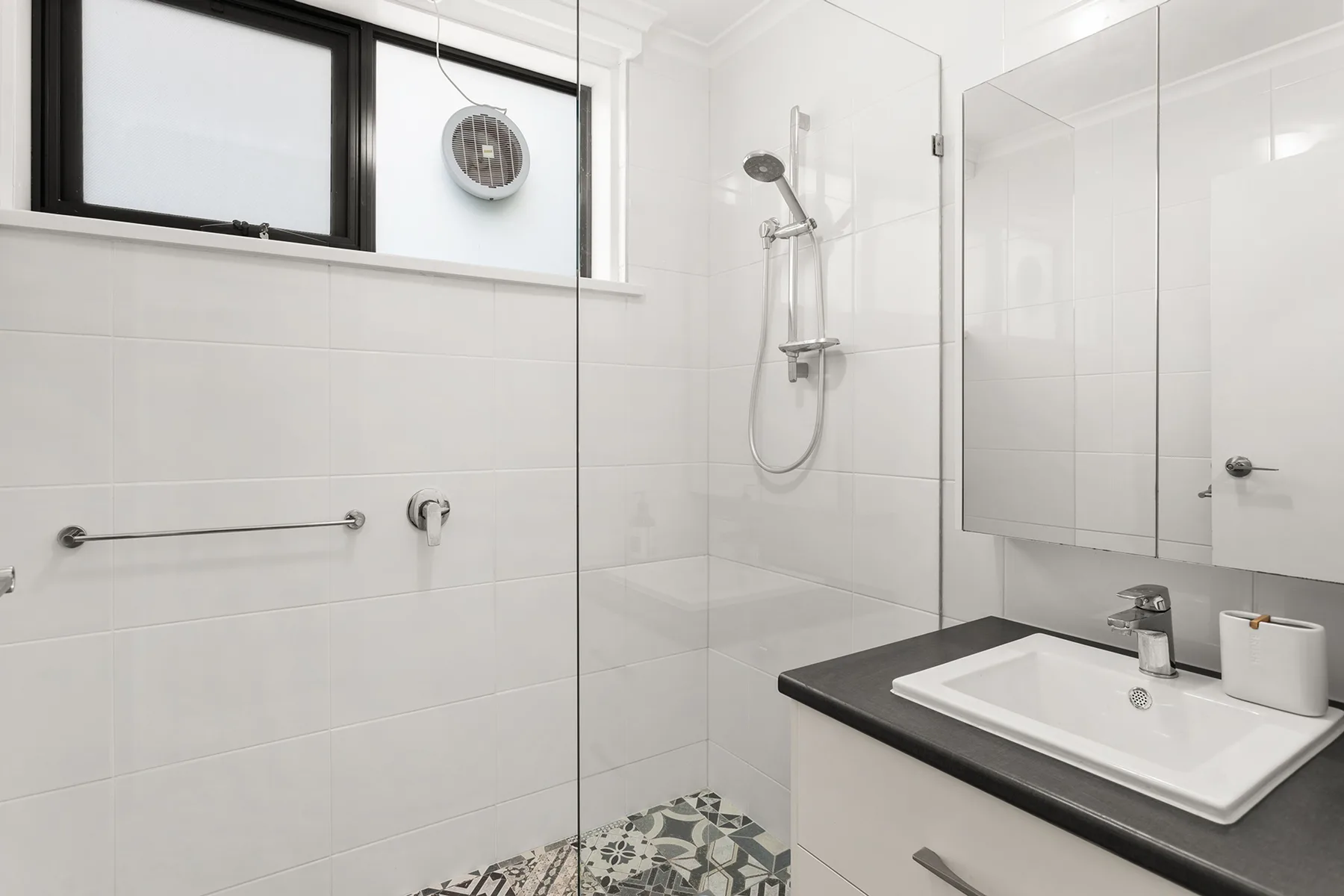 A bright tiled bathroom with a glass shower and a vanity.