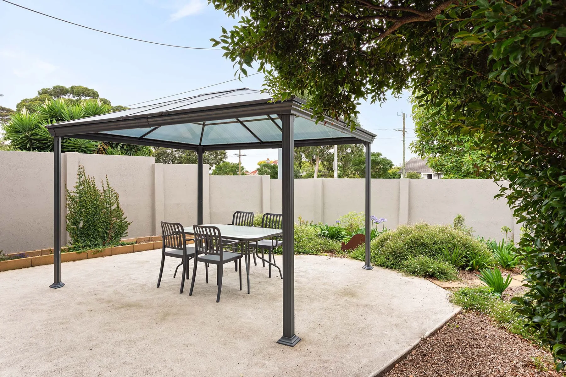 A paved outdoor patio with a covered seating area and garden beds.