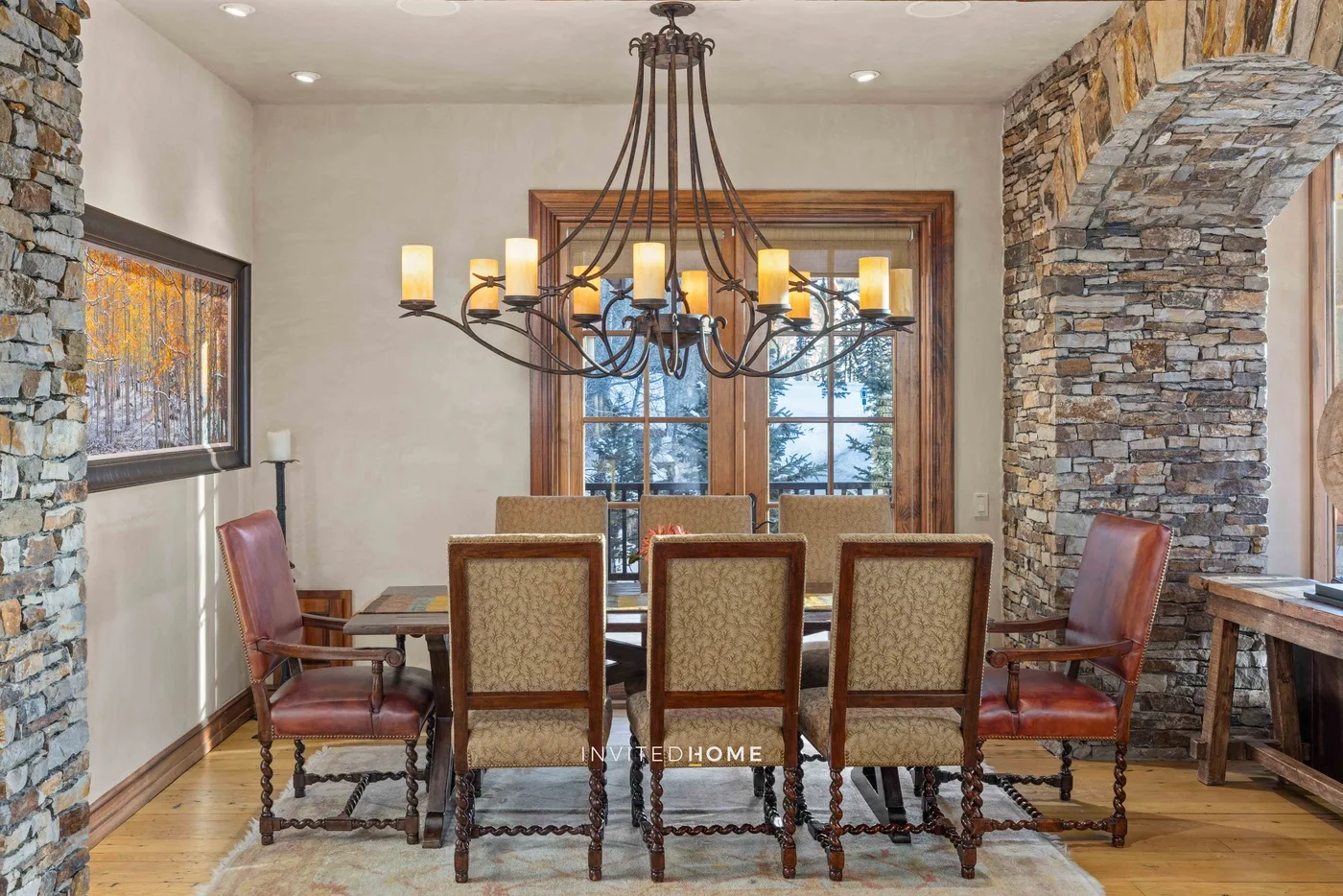 A dining room with a long table, upholstered seating, and a chandelier.