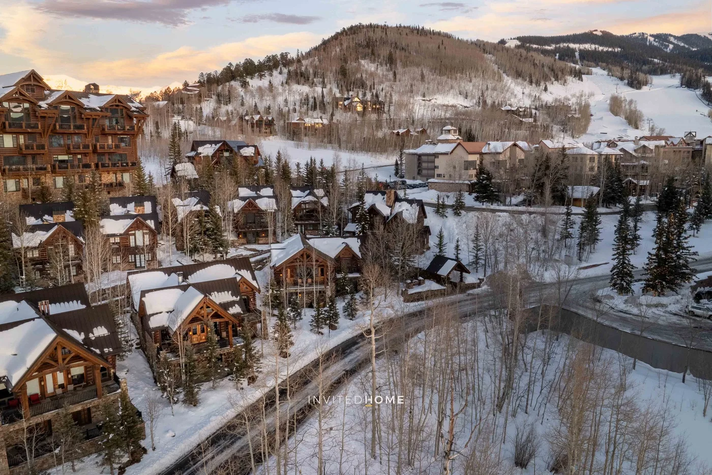 A snowy mountain resort with clustered buildings and wooded hillsides.