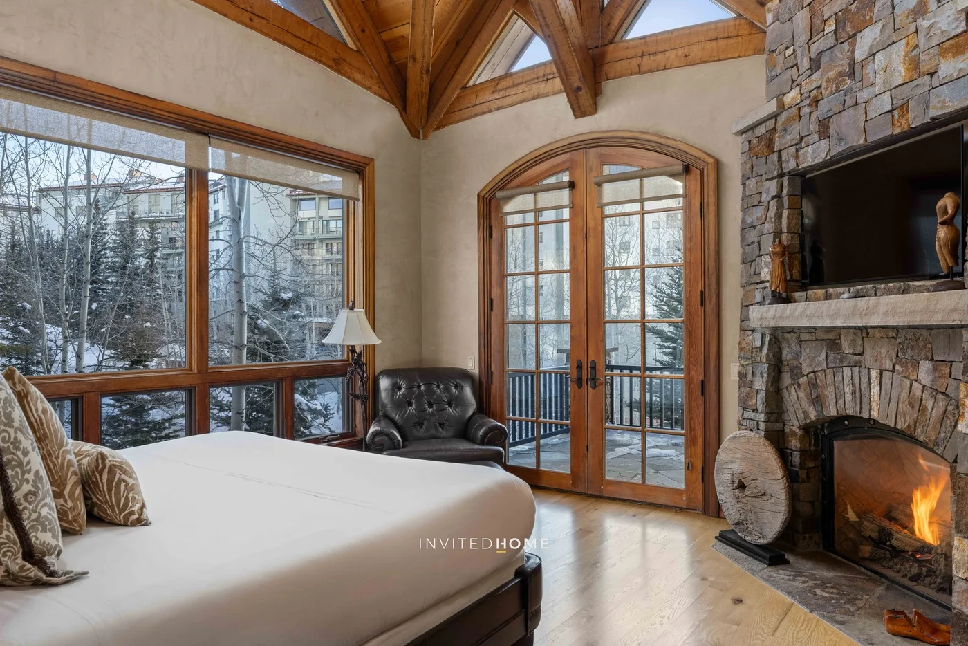 A bedroom with a bed beside large windows and a stone fireplace.