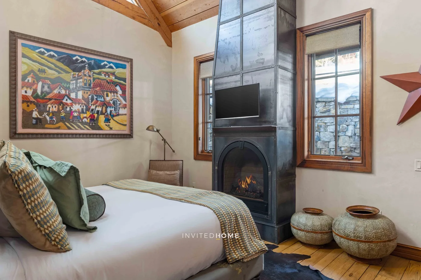 A bedroom with a bed beside a tall fireplace and television.