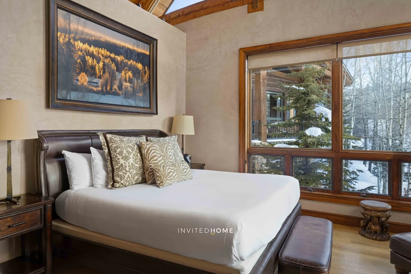 A bedroom with a bed beneath a framed picture and a large window.