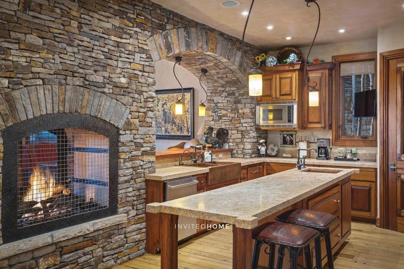 A rustic kitchen with a stone fireplace, wooden cabinets, and a central island.