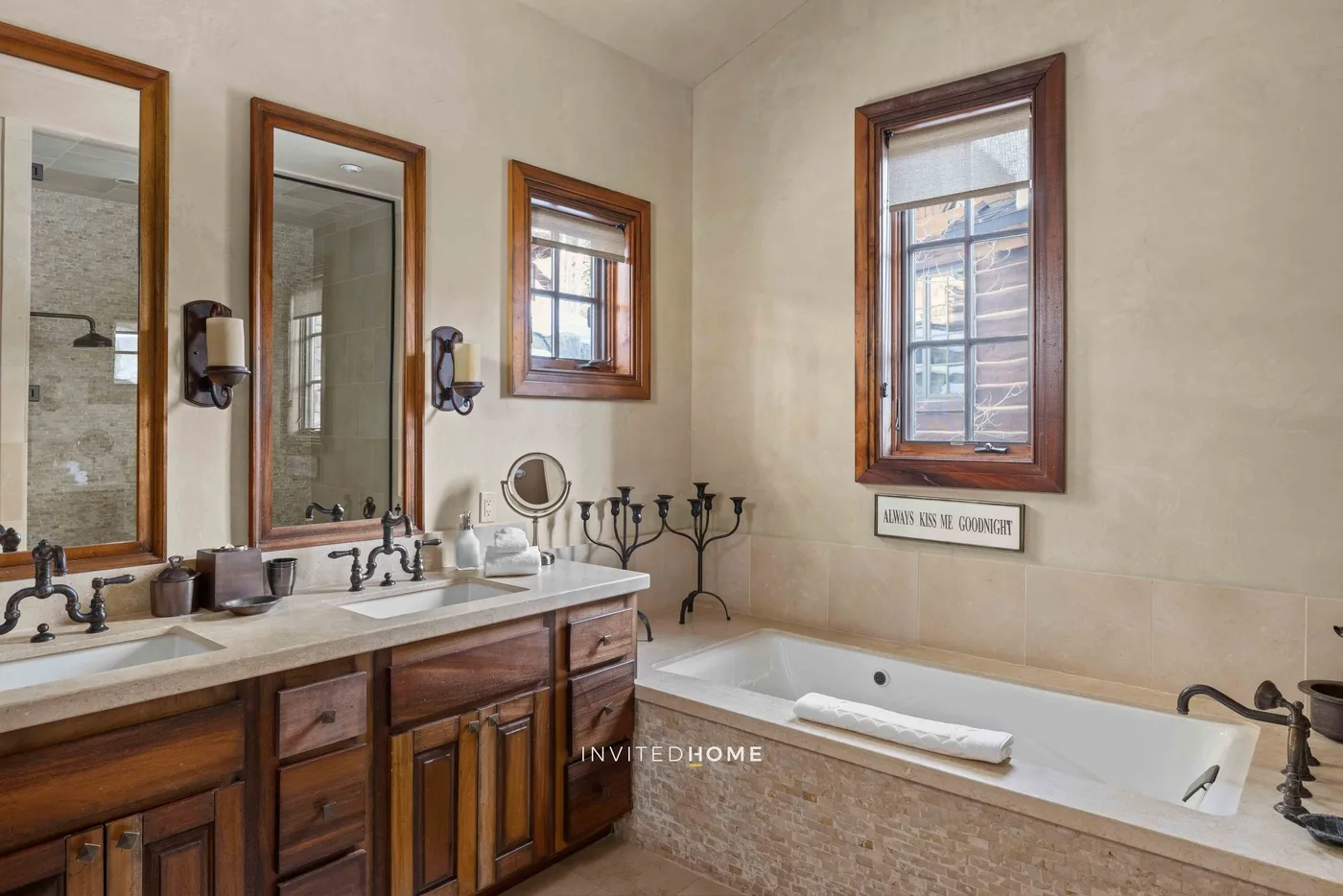 A bathroom with a long vanity, mirrors, and a bathtub beneath a window.
