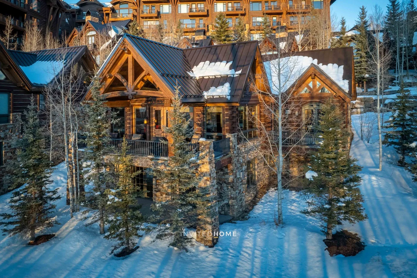 Snow-covered chalet buildings sit among evergreen trees, with a larger lodge behind them.