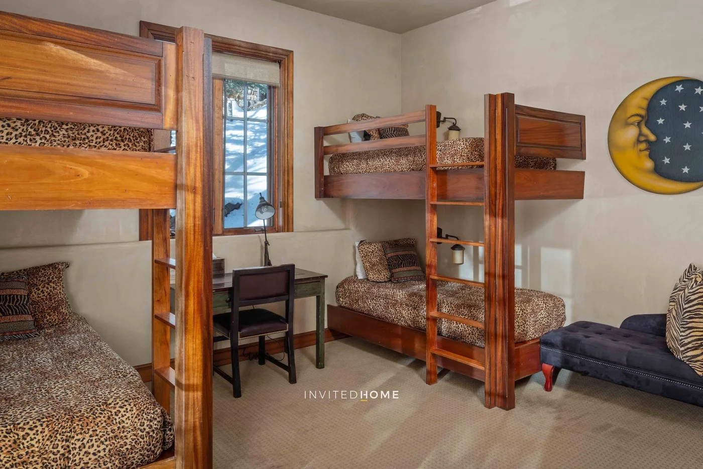 A bedroom with wooden bunk beds, patterned bedding, and a small desk by the window.