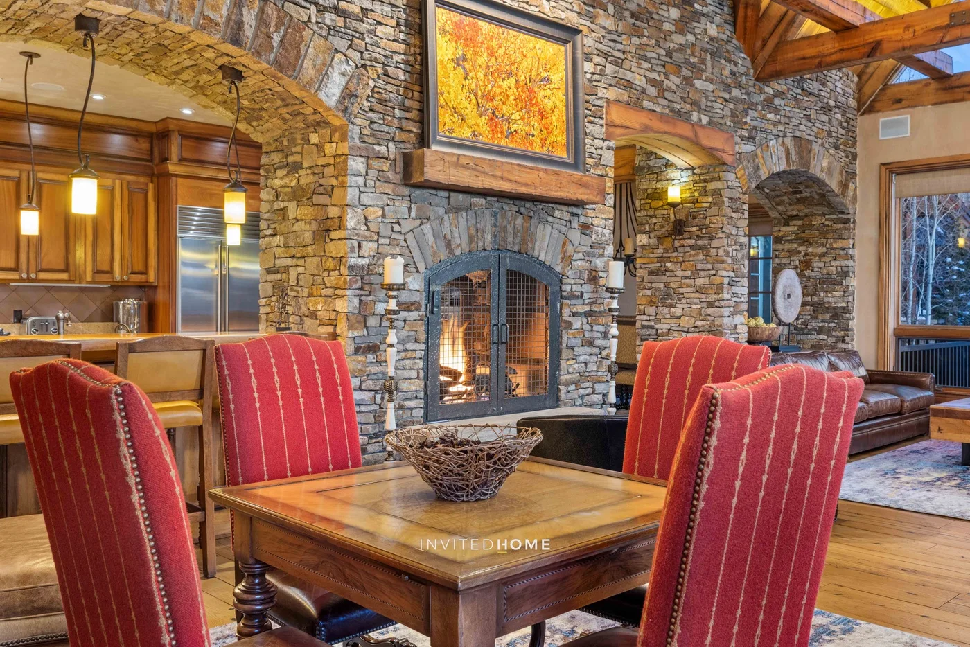 A dining area with red upholstered seating beside a stone fireplace.