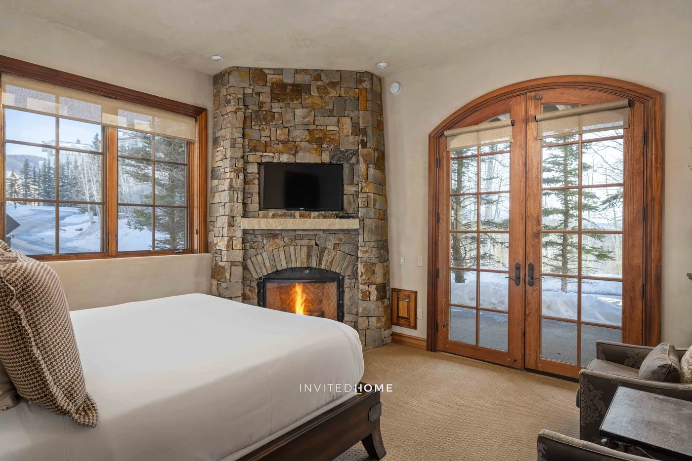 A bedroom with a bed, stone fireplace, and wood-framed windows and doors.