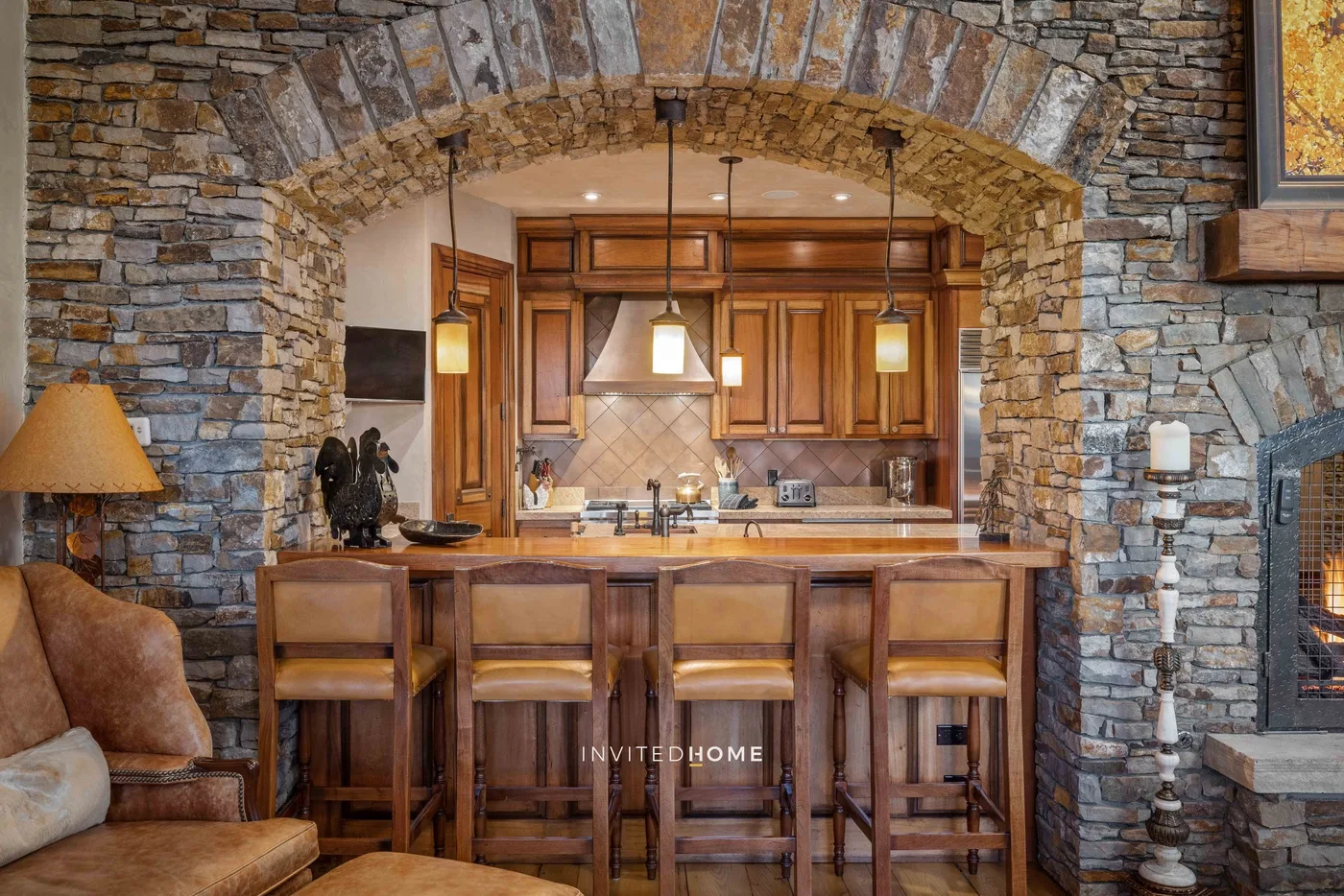 A kitchen with a wooden island sits beneath a broad stone arch.