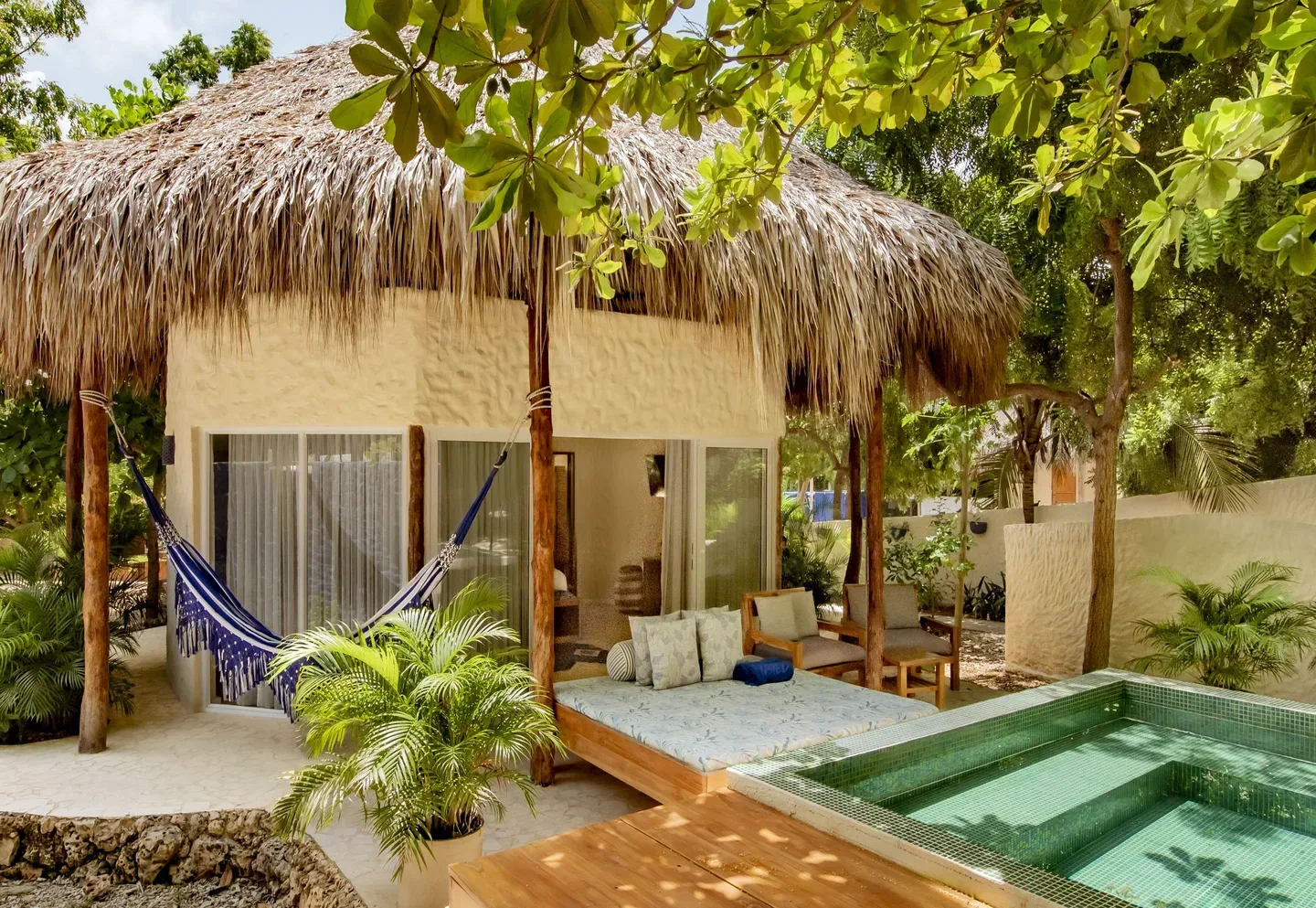 Piscina pequeña privada y hamaca fuera de una habitación con techo de paja