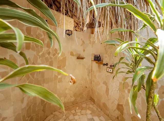 Ducha al aire libre con paredes de piedra y plantas tropicales