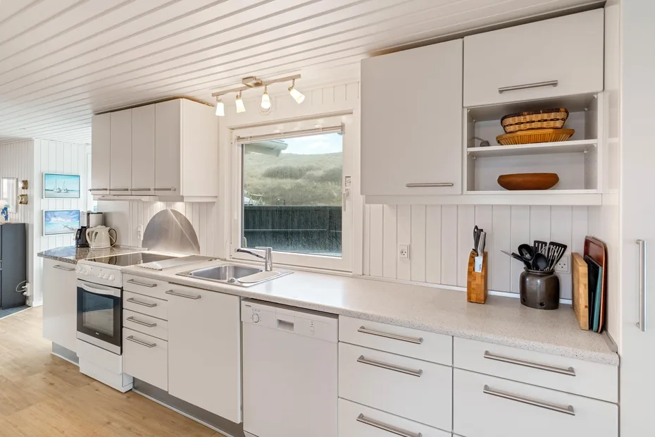 Una cocina blanca y luminosa con una encimera larga, armarios y una ventana.